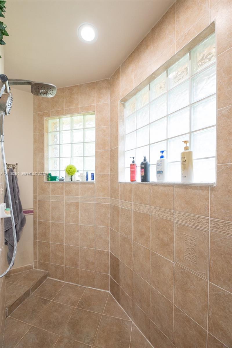 Walk-in shower featuring floor-to-ceiling tile, decorative accent trim, glass block windows, and a stainless steel shower head