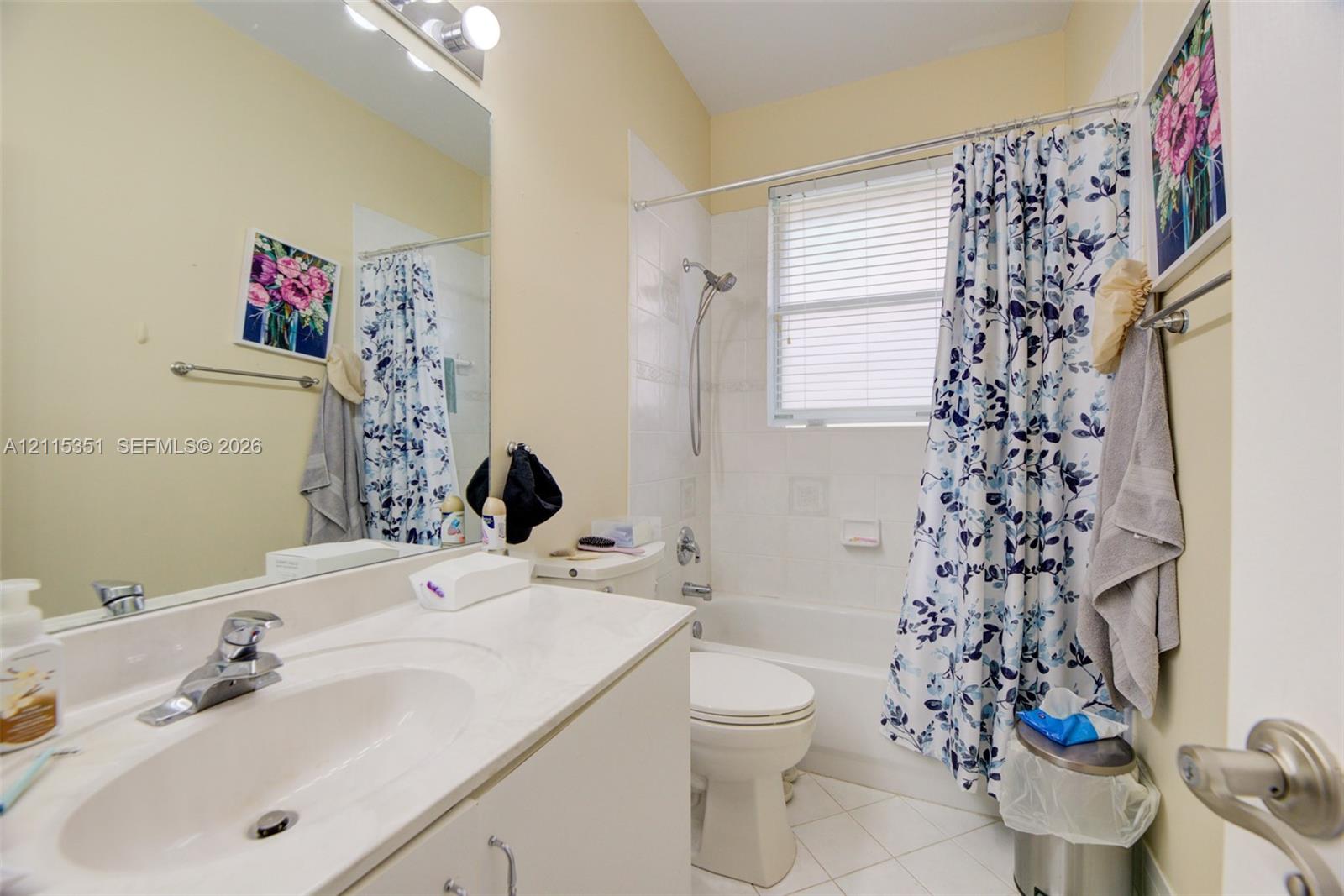 Bathroom featuring a solid-surface vanity countertop, an integrated sink with a chrome faucet, a wall-to-wall mirror, a porcelain tub-and-shower combination, and tiled flooring