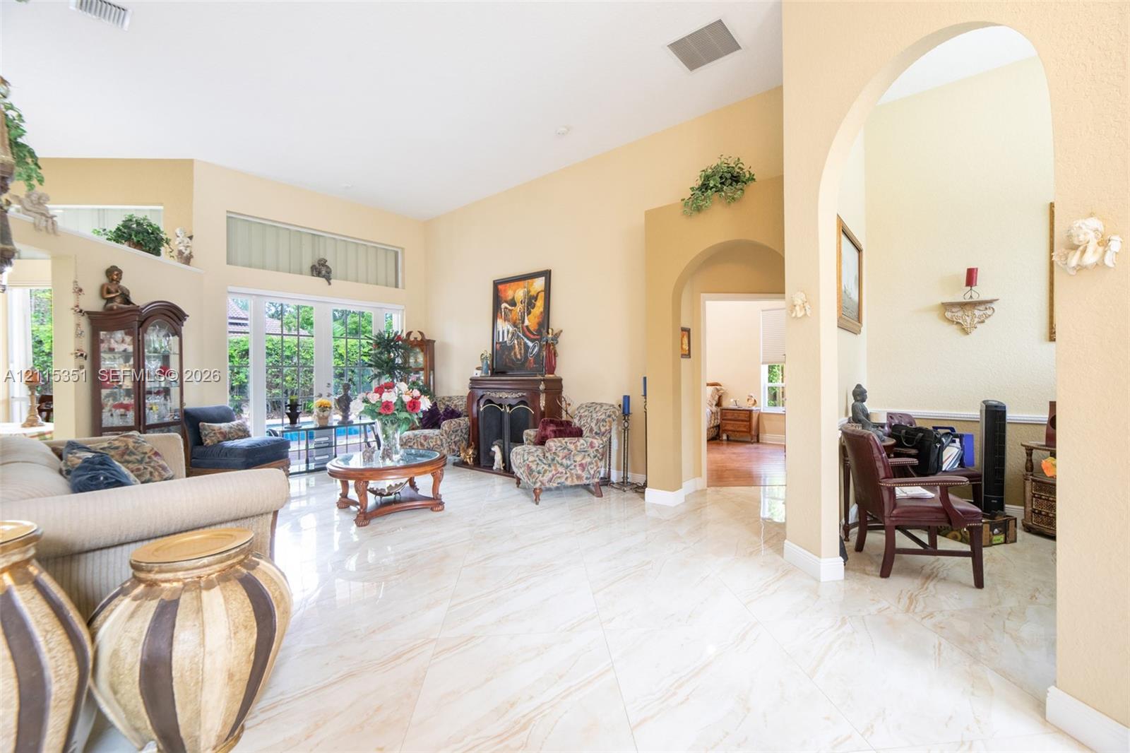 Living area featuring high ceilings, large-format tile flooring, a fireplace with a decorative mantel, arched entryways, and floor-to-ceiling windows Living area featuring high ceilings, large-format tile flooring, a fireplace with a decorative mantel, arched entryways, and floor-to-ceiling windows
