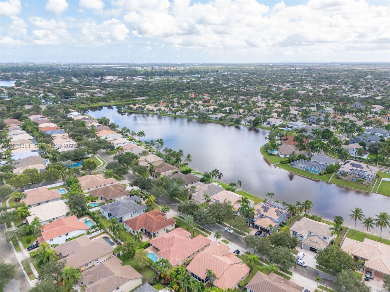 Aerial perspective of a lakeside community featuring mature palm trees and residential properties with multi-pitch tiled roofing