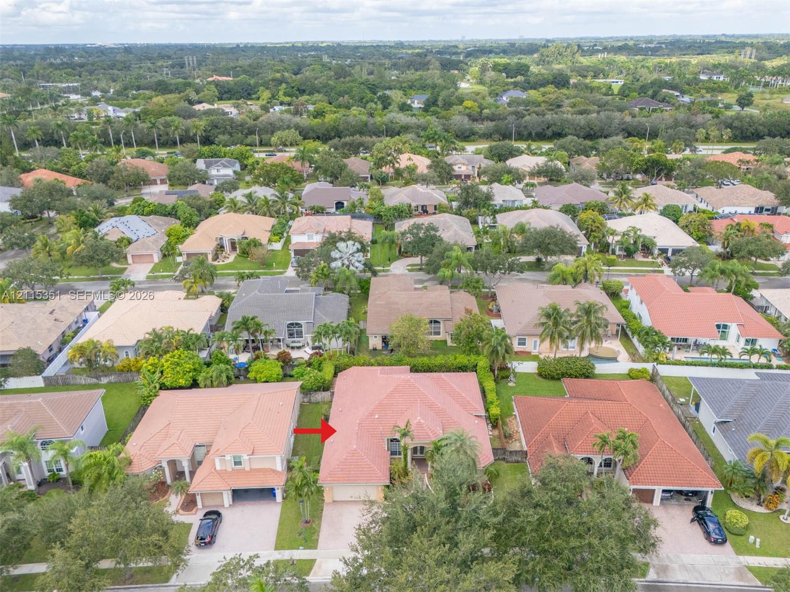 Aerial perspective of the property featuring a tile roof, multi-car garage, concrete driveway, and established landscaping