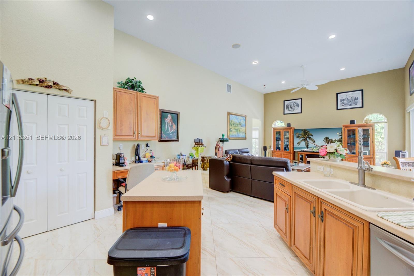 Open-concept area featuring vaulted ceilings, tile flooring, wood cabinetry, a center island with countertop seating, and recessed lighting
