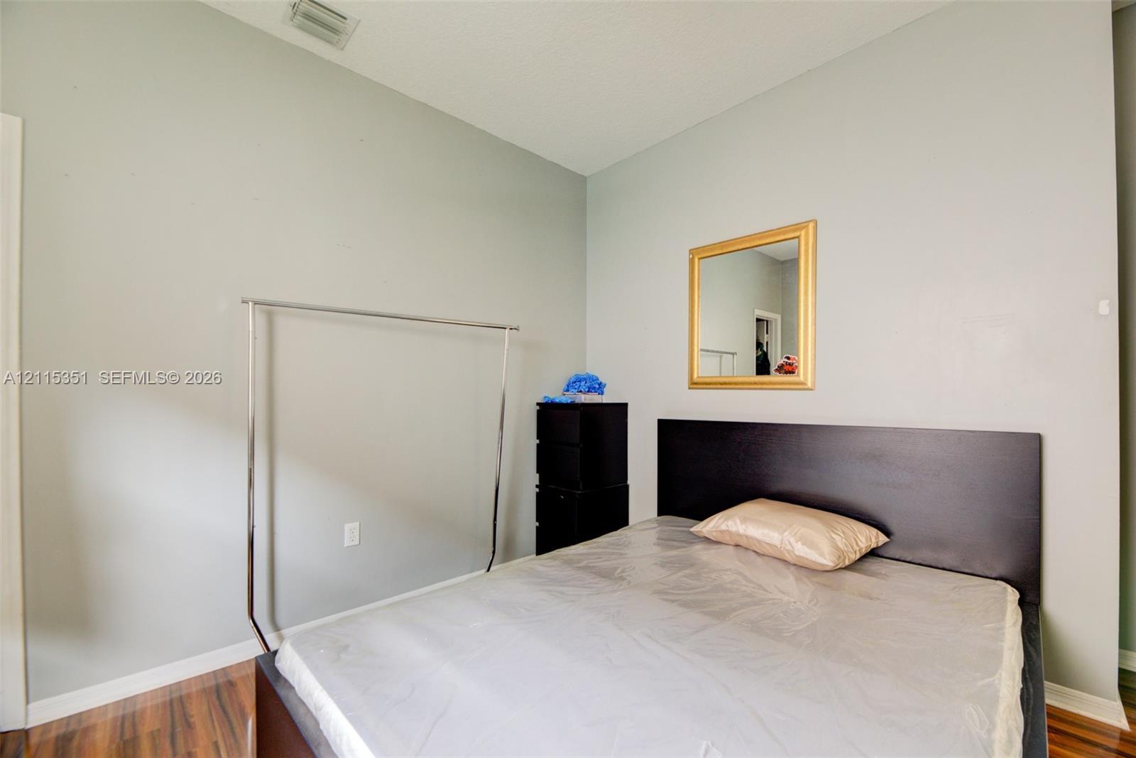High-ceilinged room with wood-finish flooring and a wall-mounted mirror