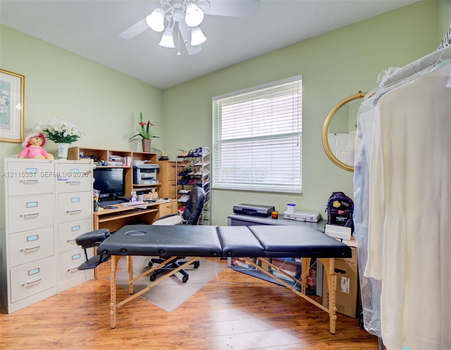 Room featuring wood-finish flooring, a ceiling-mounted light fixture with four glass shades, and a single-pane window with horizontal blinds