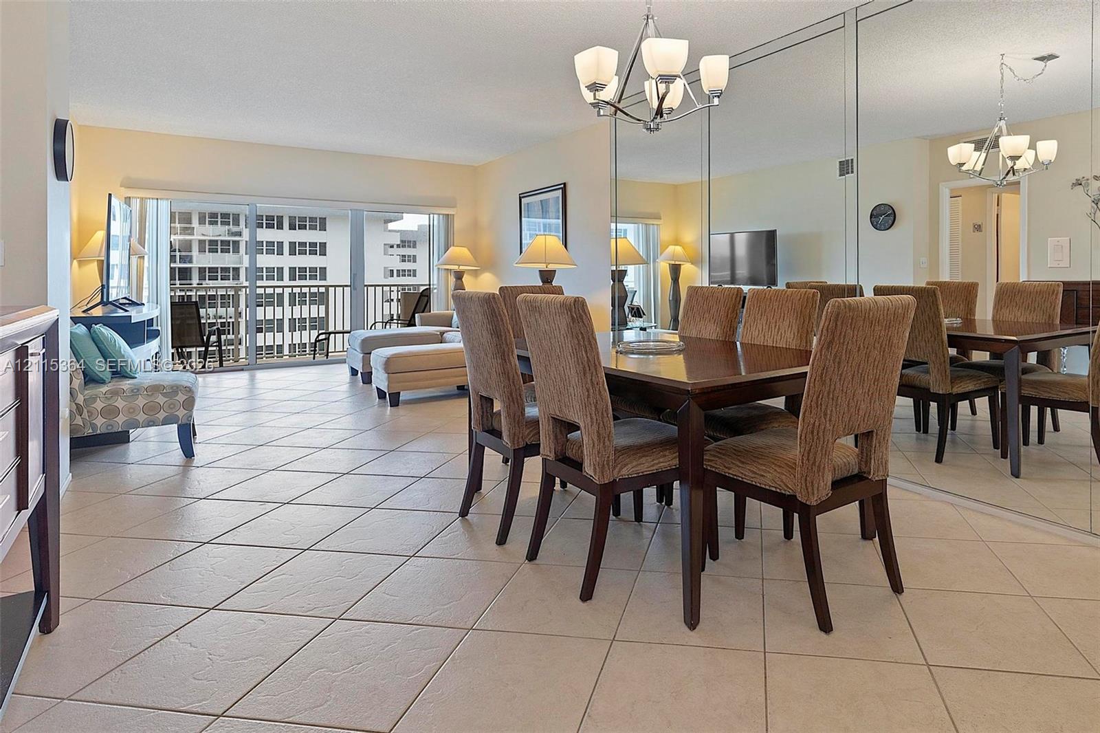 Open-concept dining area featuring large-format diagonal tile flooring, floor-to-ceiling mirrored wall accents, and an overhead multi-arm chandelier