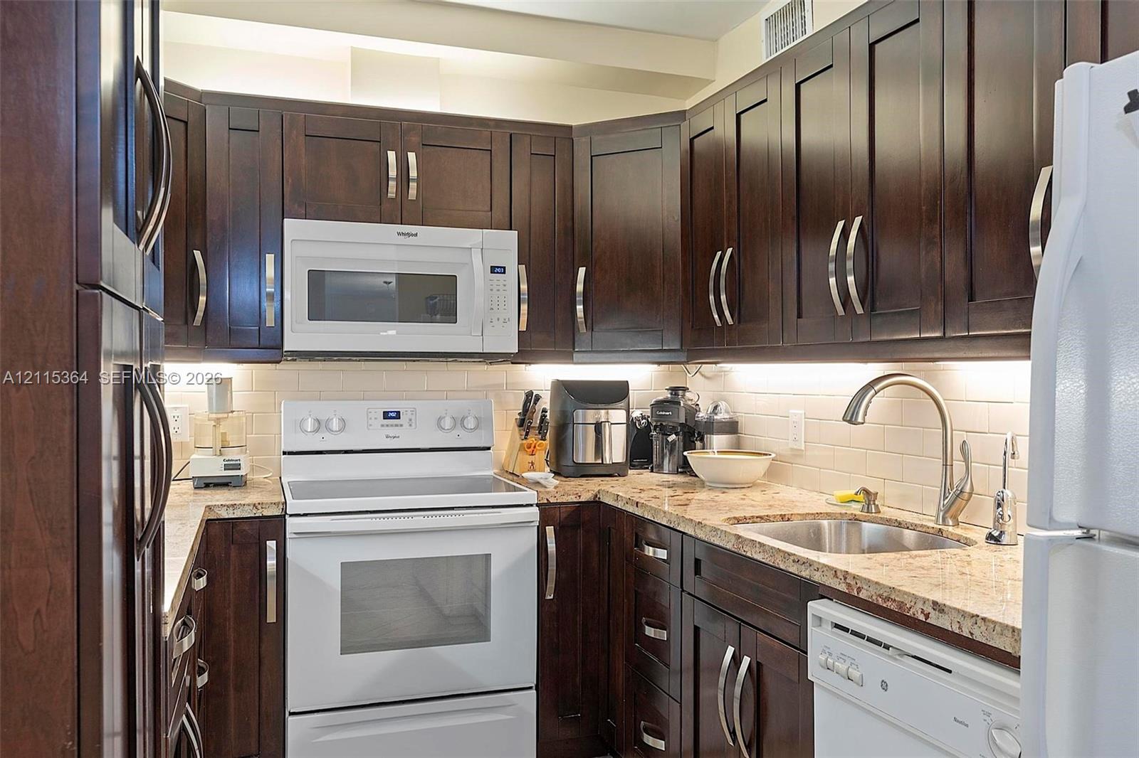 Kitchen featuring dark wood-finish cabinetry, stone countertops, a light-toned subway tile backsplash, and under-cabinet task lighting