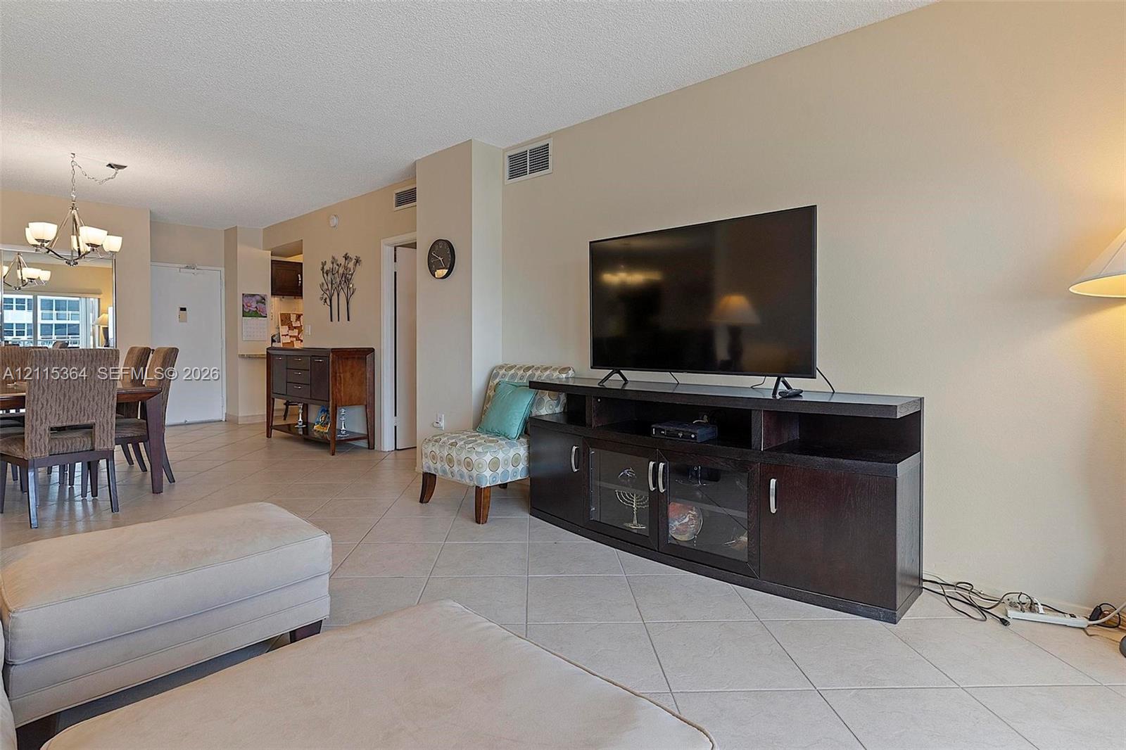 Neutral-toned interior space featuring light-colored diagonal floor tile and a multi-arm suspended chandelier
