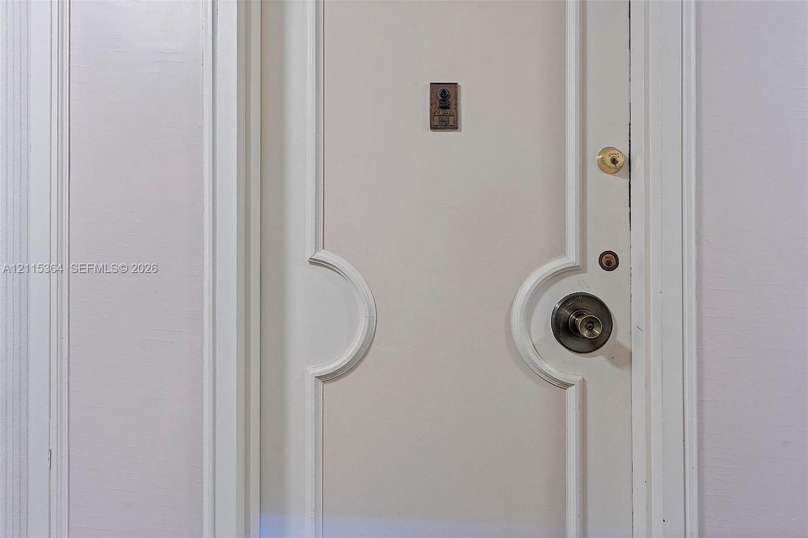 White interior door featuring recessed arched paneling, brushed metallic hardware, a deadbolt, and an integrated door viewer