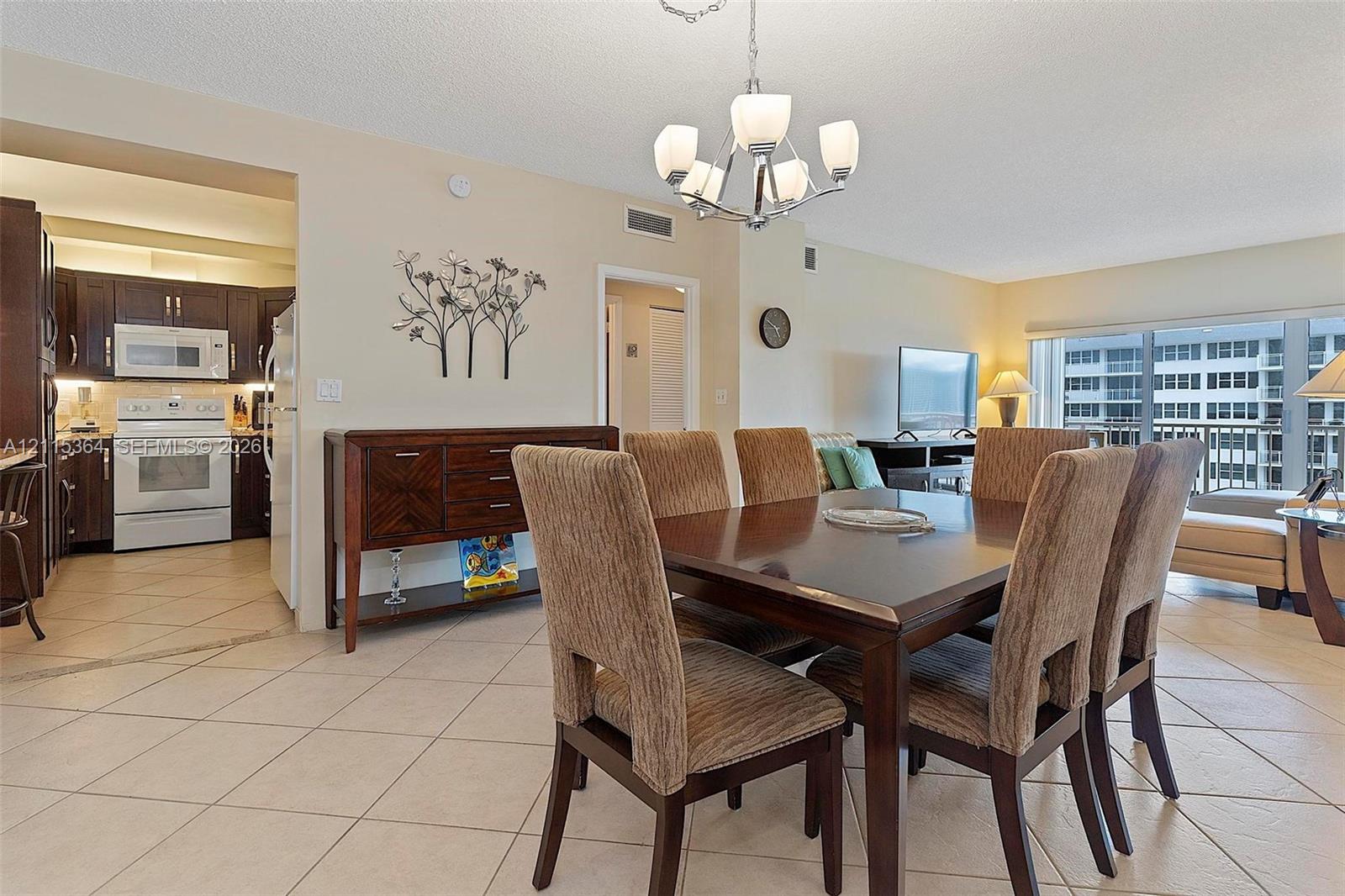 Open concept area featuring large-format ceramic tile flooring, a multi-arm chandelier, and a kitchen with dark-toned cabinetry and white appliances