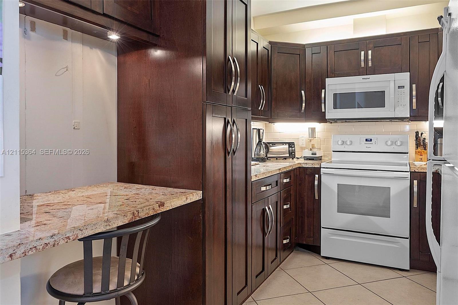 Kitchen featuring dark wood cabinetry, stone countertops, tiled flooring, under-cabinet lighting, and built-in appliances