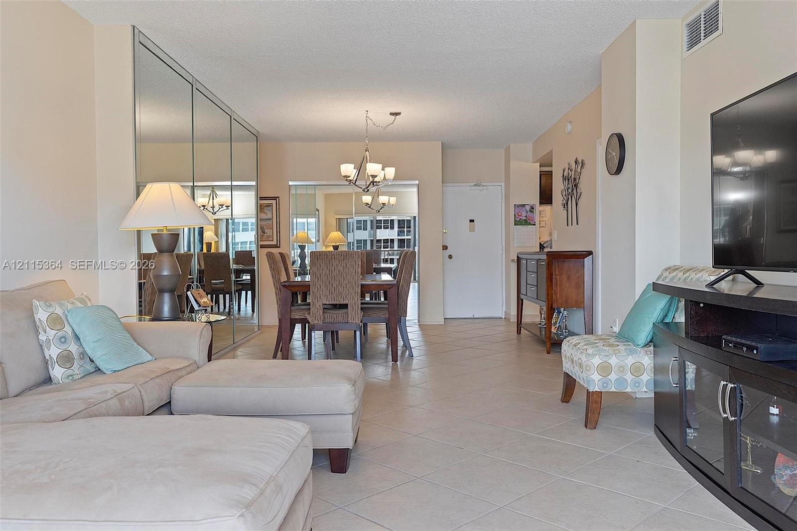 Open-concept interior featuring large-format tile flooring, wall-to-wall mirrored closet doors, a multi-arm chandelier, and neutral wall tones