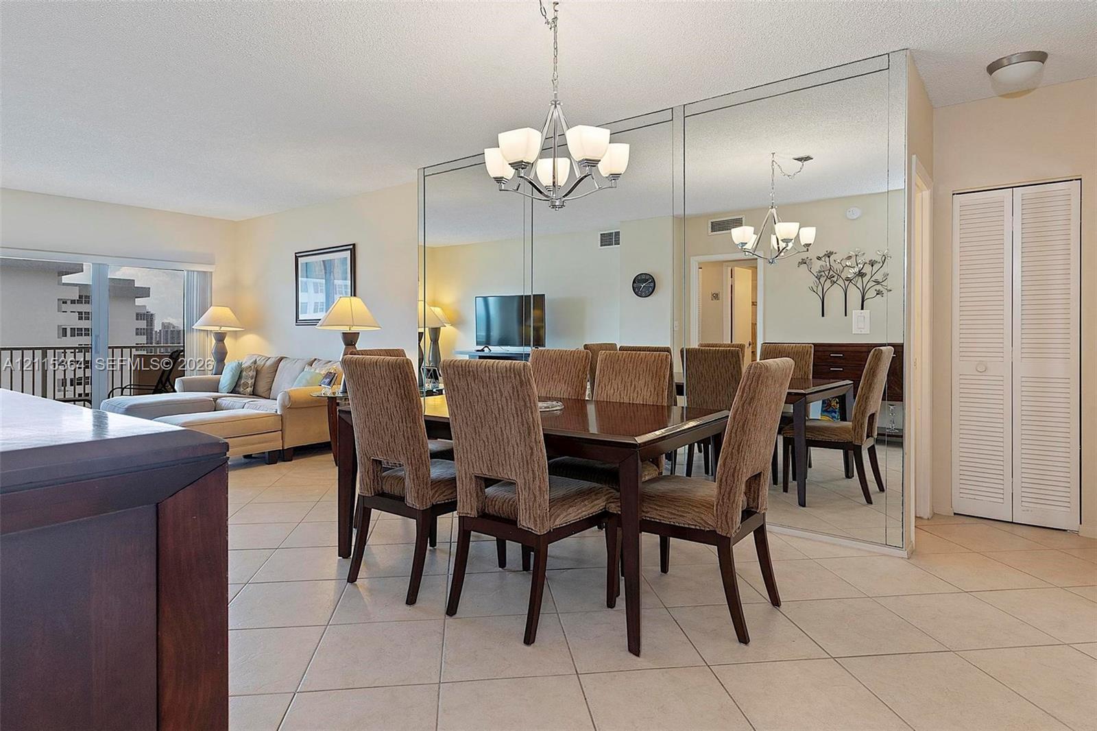 Dining area featuring tile flooring, floor-to-ceiling wall mirrors, a multi-arm chandelier, and white louvered closet doors