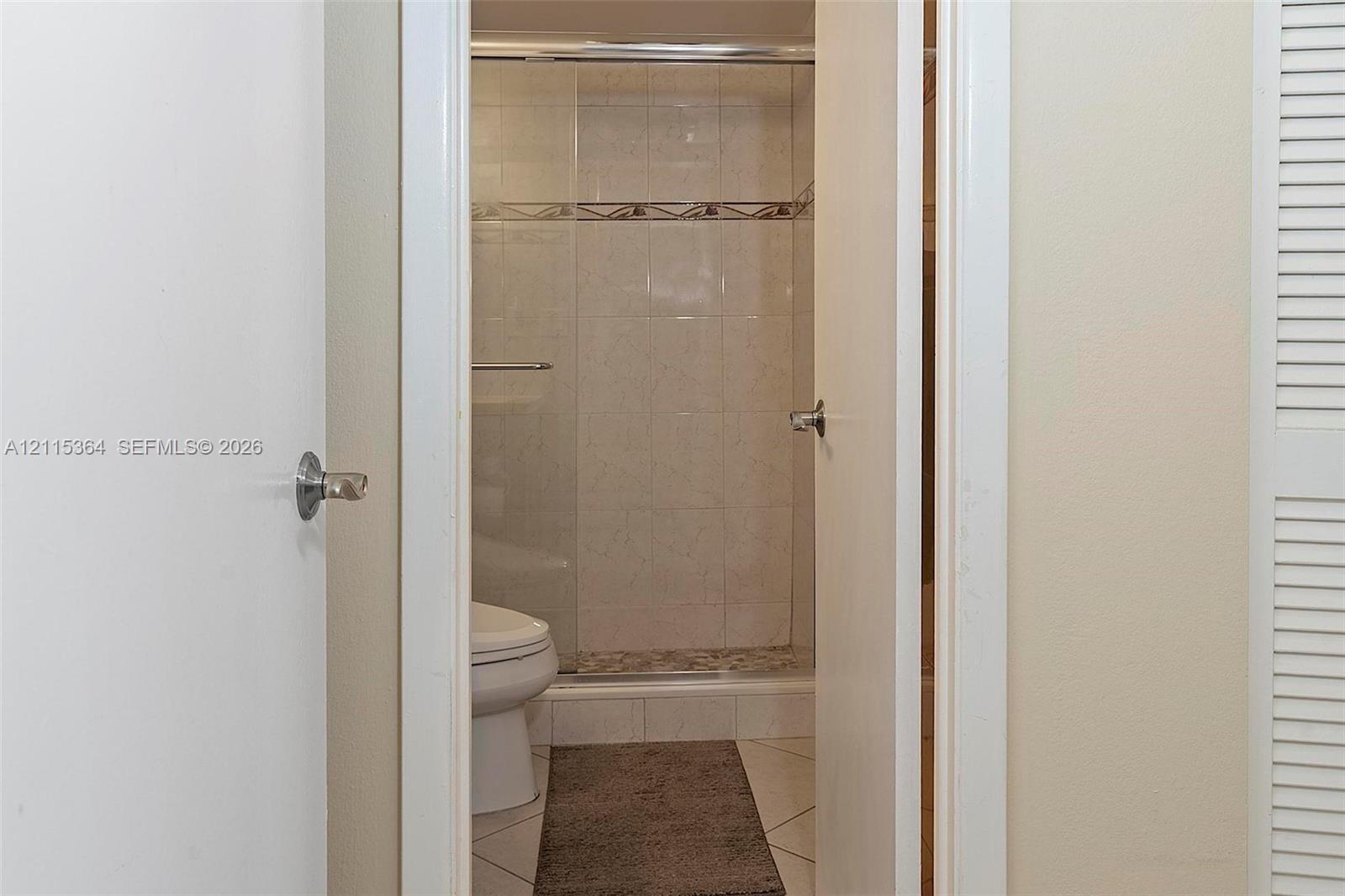 Bathroom featuring a glass-enclosed shower, light-toned wall tiling with decorative accent trim, and light-toned tile flooring