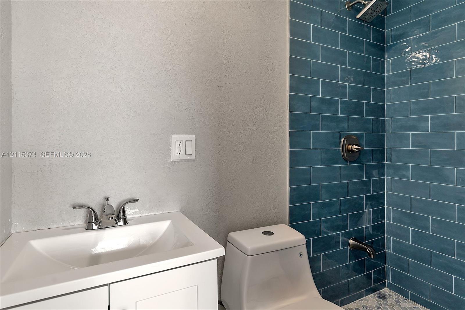 Bathroom featuring a white vanity cabinet, polished chrome faucet, dual-flush toilet, blue subway tile shower surround, and mosaic tile flooring