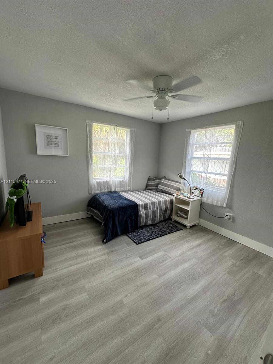 Room featuring neutral wall paint, wood-finish flooring, dual windows, and a ceiling-mounted fan