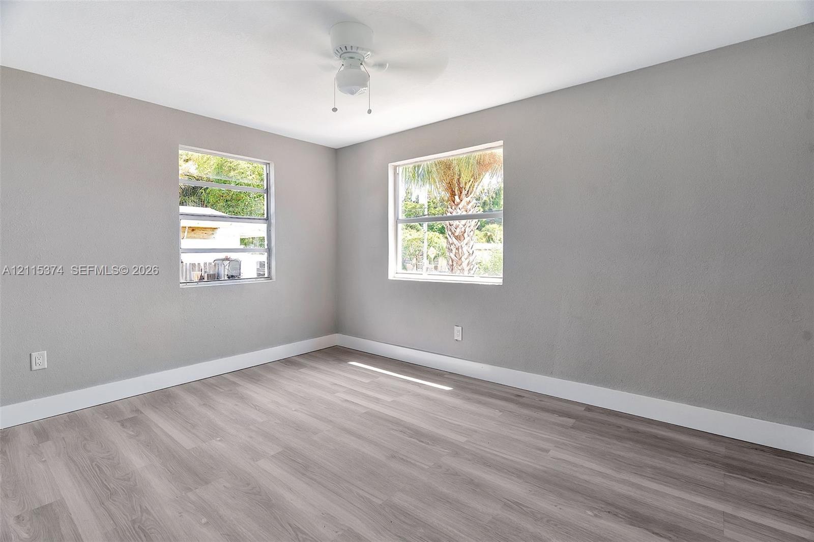Neutral-toned walls, wood-finish flooring, two dual-pane windows, and a ceiling fan with integrated lighting
