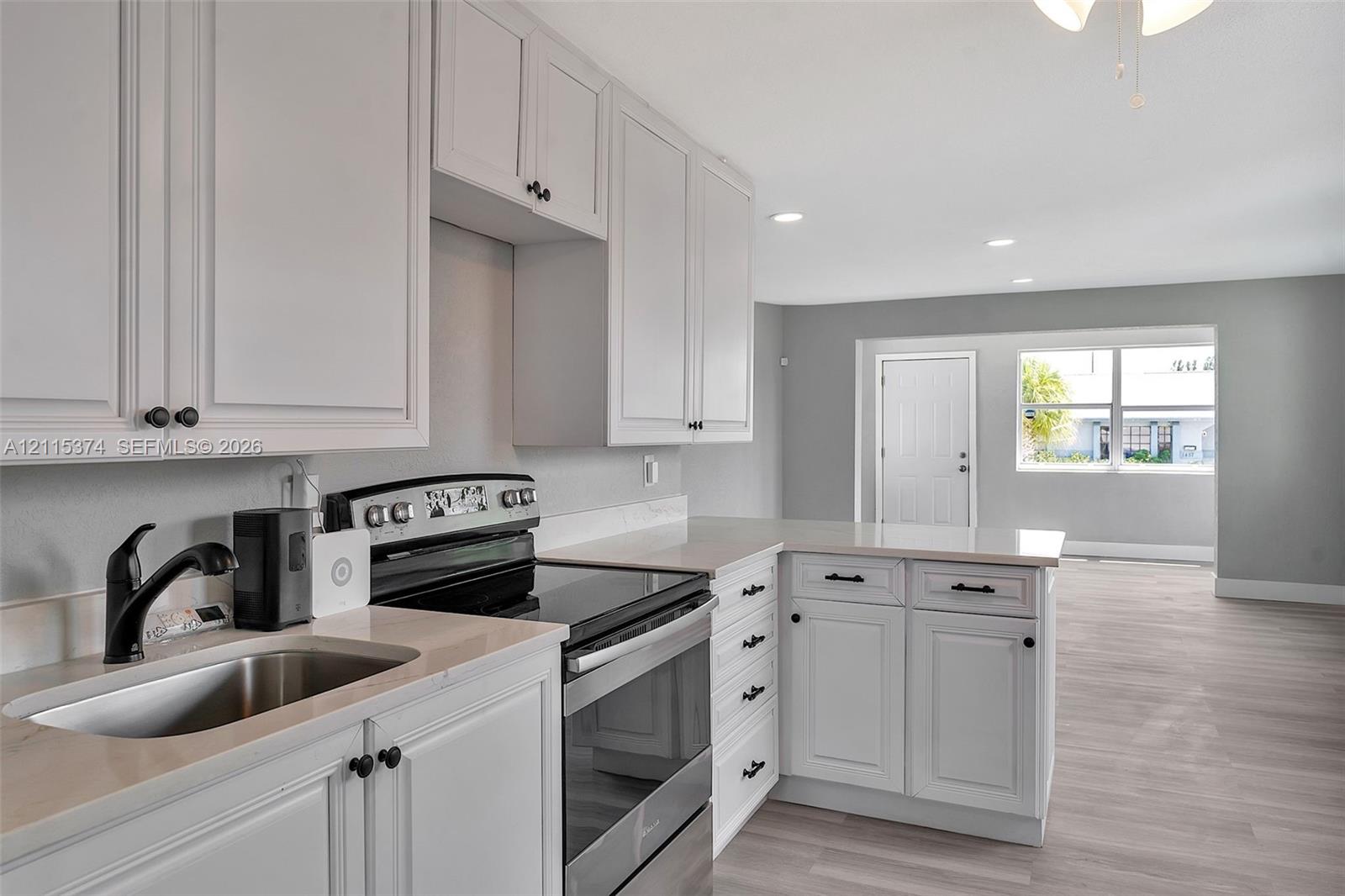 Kitchen featuring white shaker-style cabinetry, light-toned stone-finish countertops, stainless steel appliance suite, recessed lighting, and wood-finish flooring