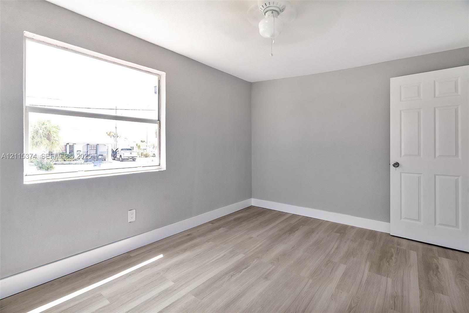 Neutral grey walls, wood-finish flooring, white six-panel interior door, and a ceiling-mounted light fixture
