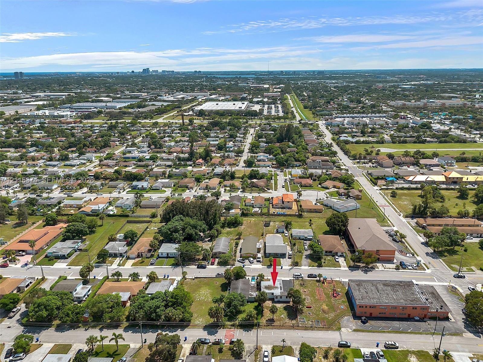 Aerial perspective of a detached residential property situated on a corner lot, featuring a flat roof and surrounding landscape with mature trees