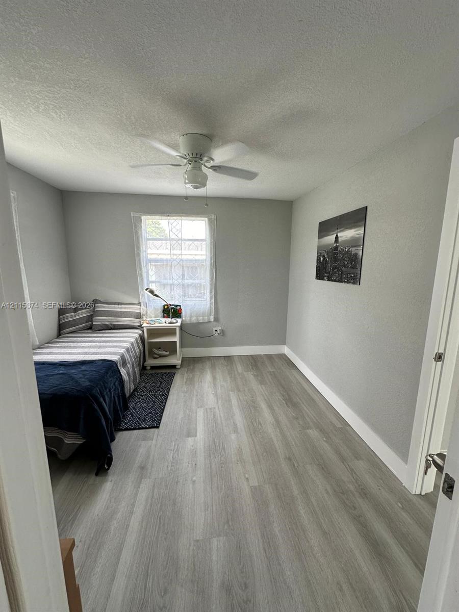 Neutral-toned interior featuring wood-finish flooring, a white ceiling fan with integrated lighting, and a single-pane window