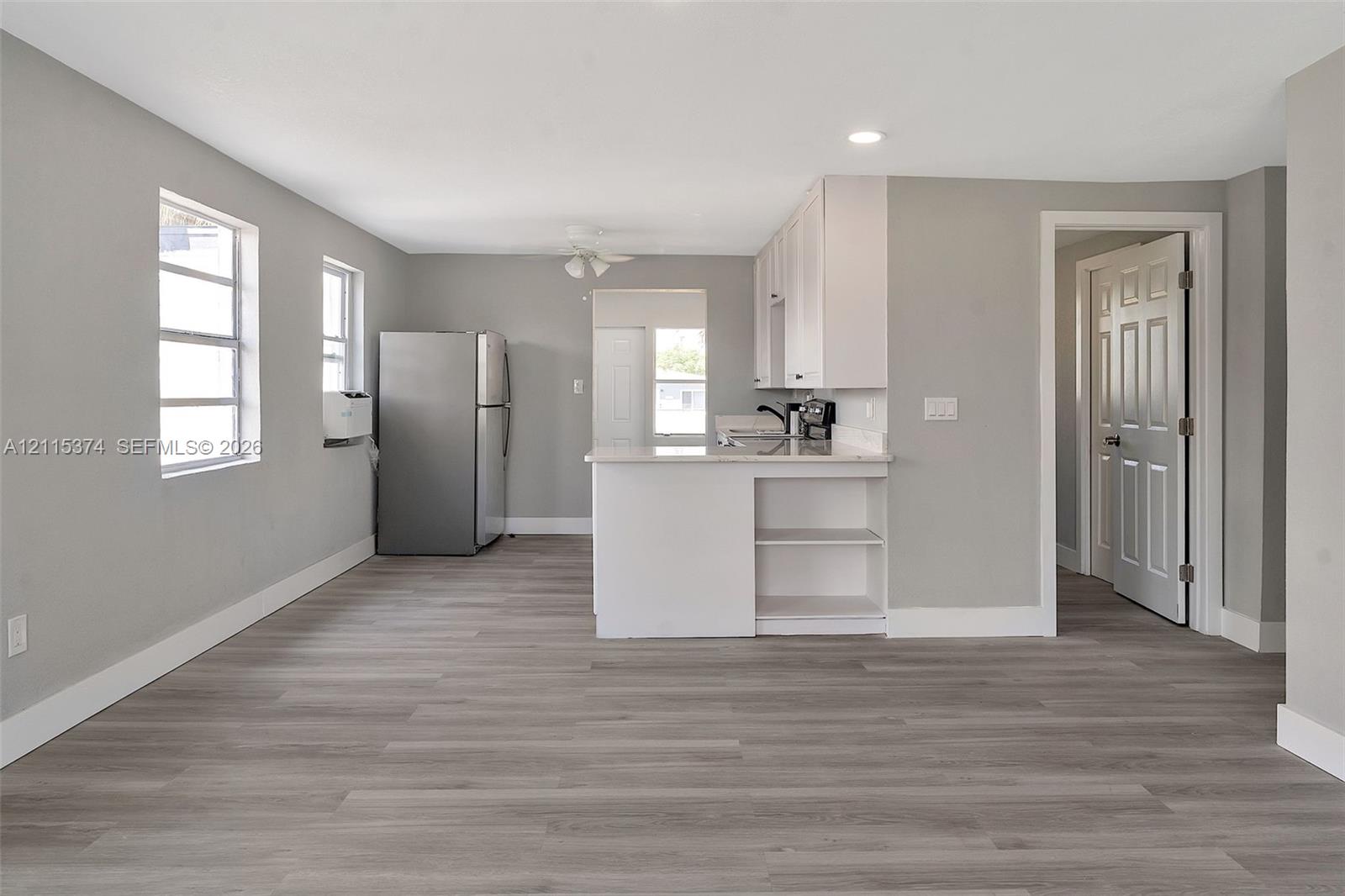 Kitchen featuring wood-finish flooring, white cabinetry, a peninsula with integrated shelving, and stainless steel refrigerator