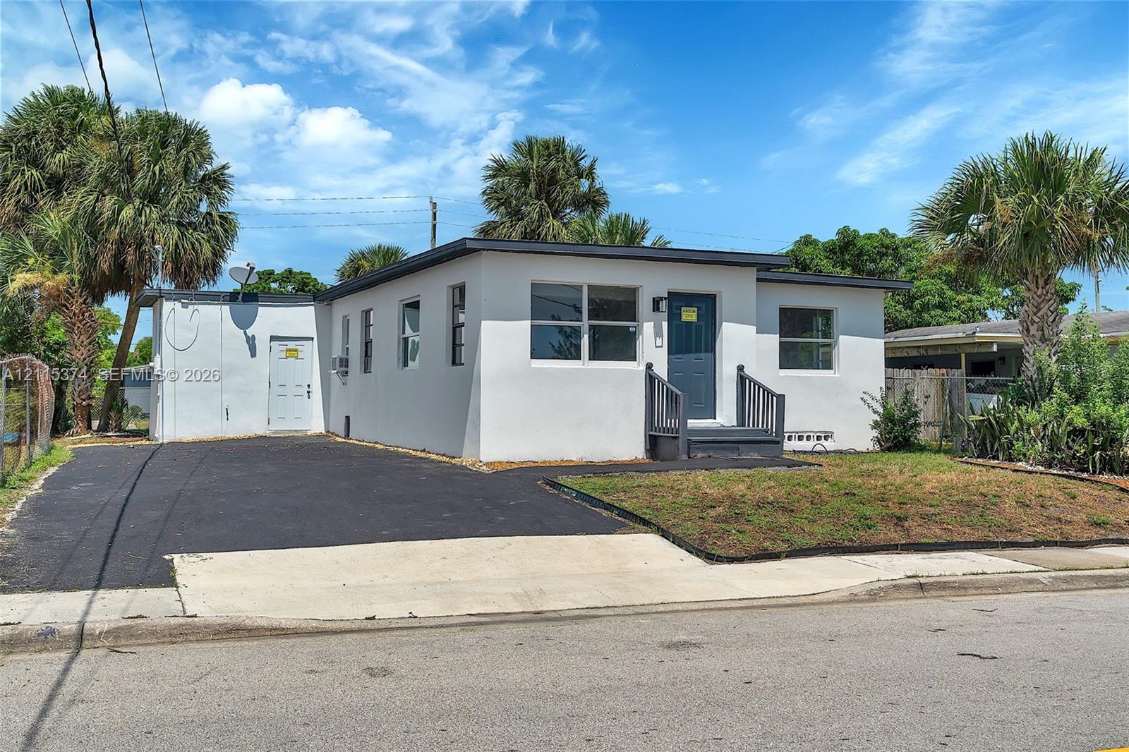 Single-story exterior featuring white stucco siding, a flat roofline, an asphalt-paved driveway, multi-pane windows, and a dark-finished entryway with stairs