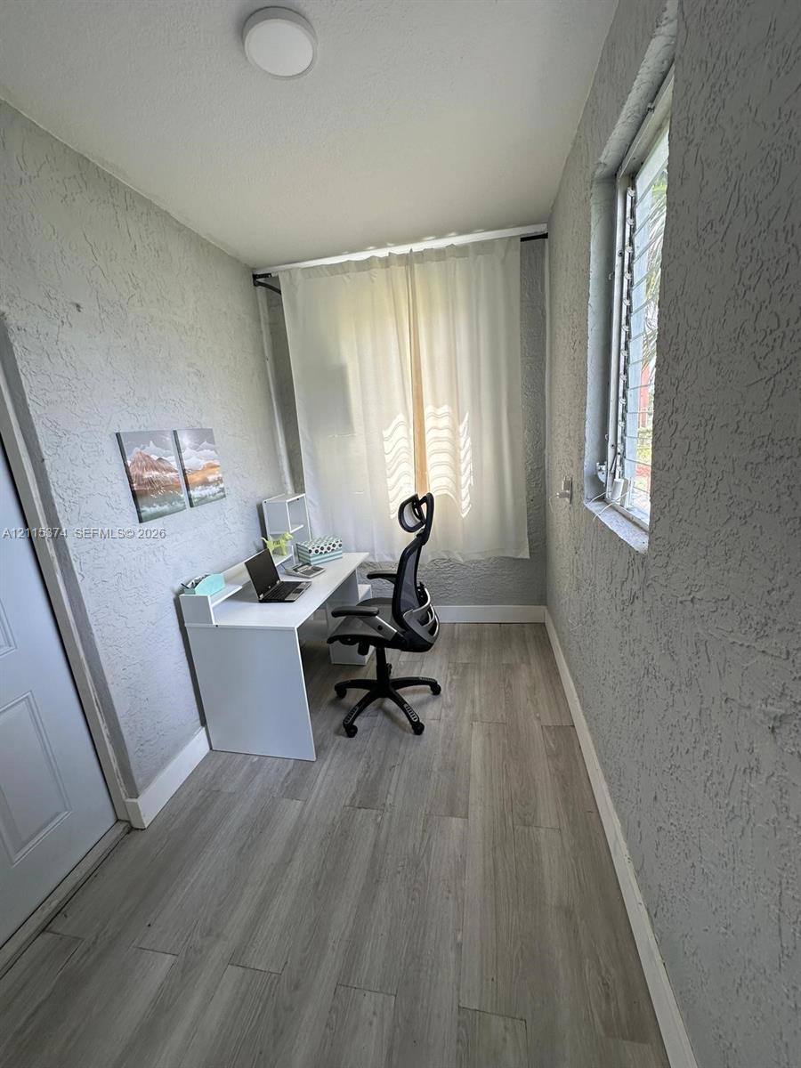 Room featuring wood-finish flooring, textured wall finishes, and a window with louvered glass panes