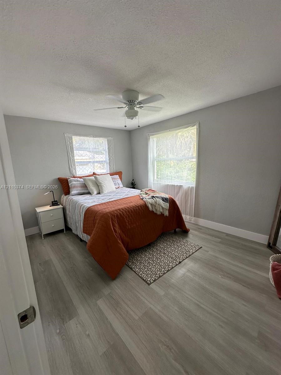 Neutral-toned walls, wood-finish flooring, dual windows with natural light, and a white ceiling fan