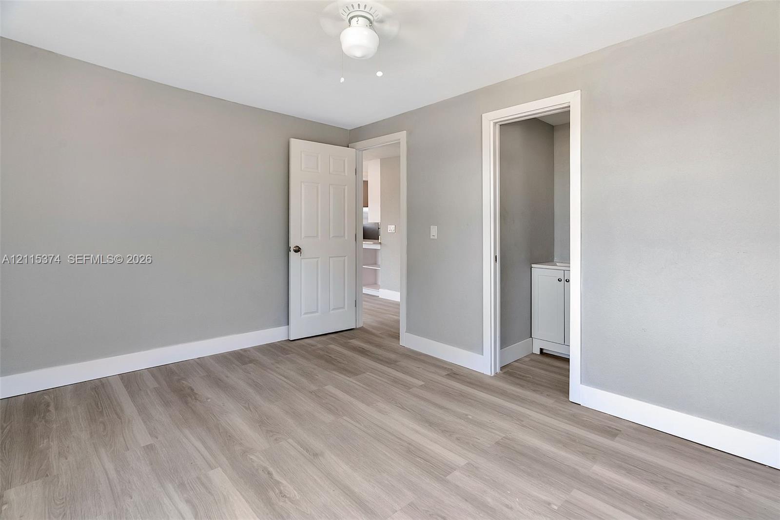 Neutral-toned interior space featuring wood-finish flooring, a ceiling-mounted light fixture, and a six-panel door