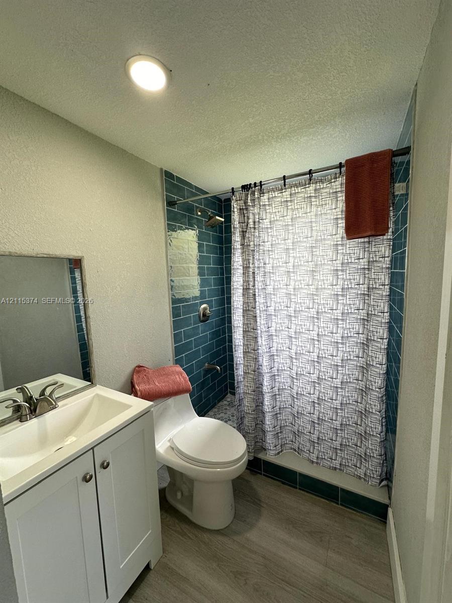 Bathroom featuring a white vanity cabinet with an integrated basin, brushed nickel faucet, blue subway tile shower surround, and wood-finish flooring