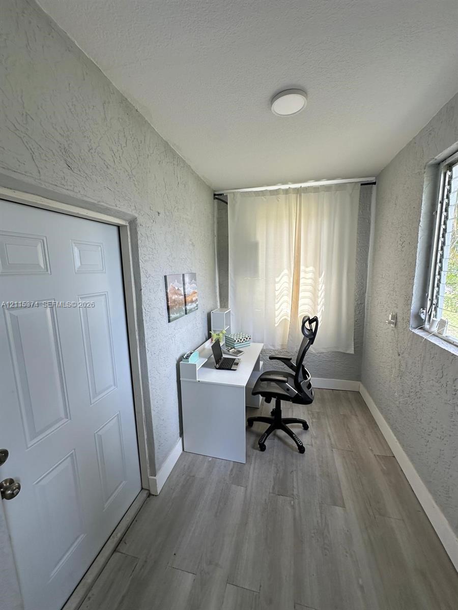 Neutral-toned wood-finish flooring, textured wall finishes, solid-core interior door with metallic hardware, and flush-mount ceiling lighting