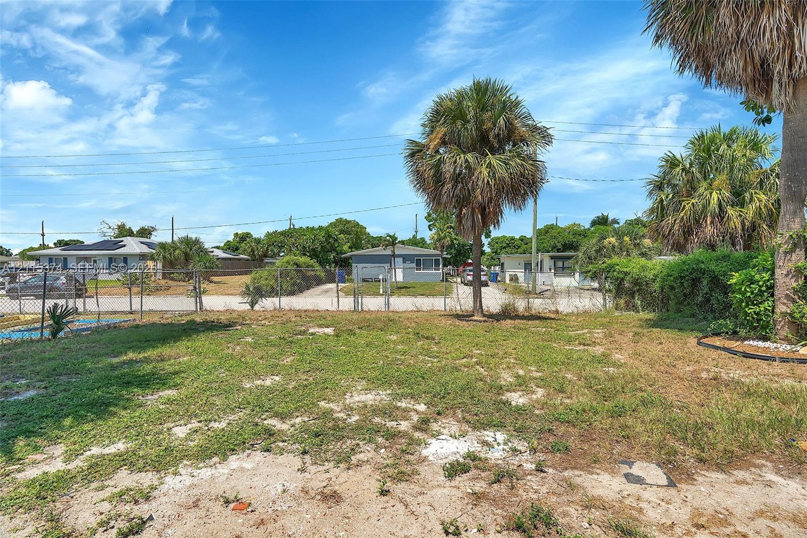 Expansive lot featuring mature palm trees and chain-link perimeter fencing