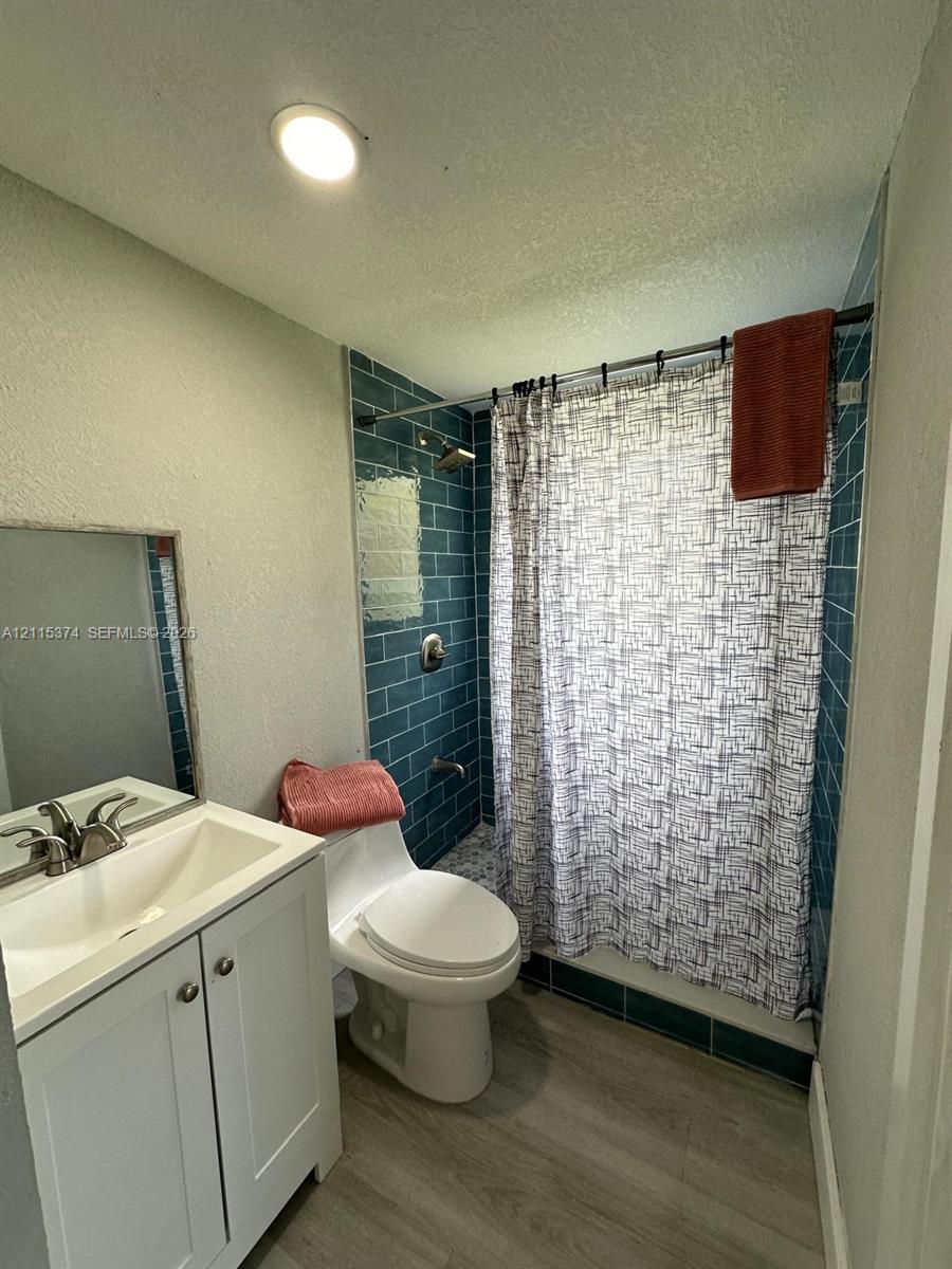 Bathroom featuring wood-finish flooring, white vanity with integrated sink, chrome-finish faucet, and blue subway-tiled shower surround