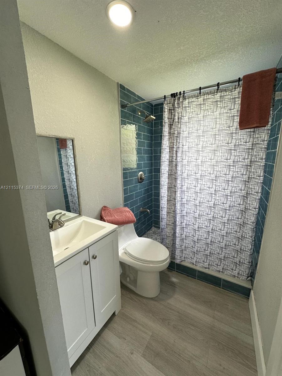 White shaker-style vanity with integrated sink, wood-finish flooring, and shower enclosure featuring blue subway-style tile surrounds