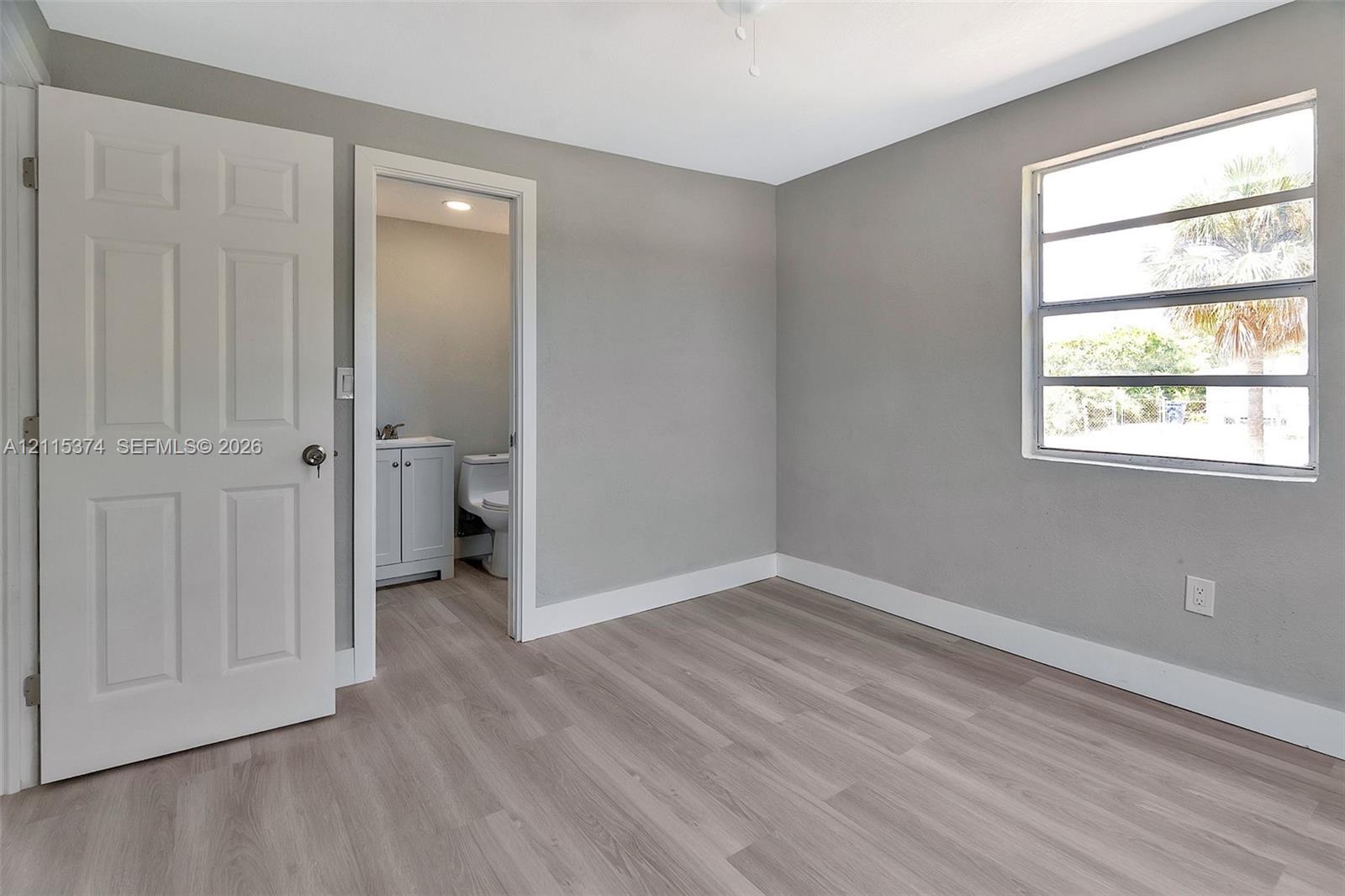 Neutral-toned interior featuring wood-finish flooring, a multi-pane horizontal window, and a white six-panel interior door