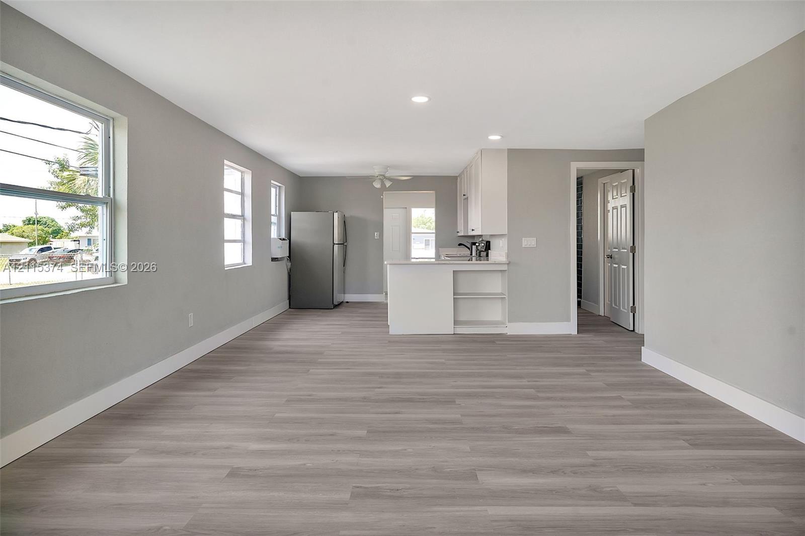 Open-concept interior featuring wood-finish flooring, recessed lighting, white cabinetry, and windows providing natural illumination