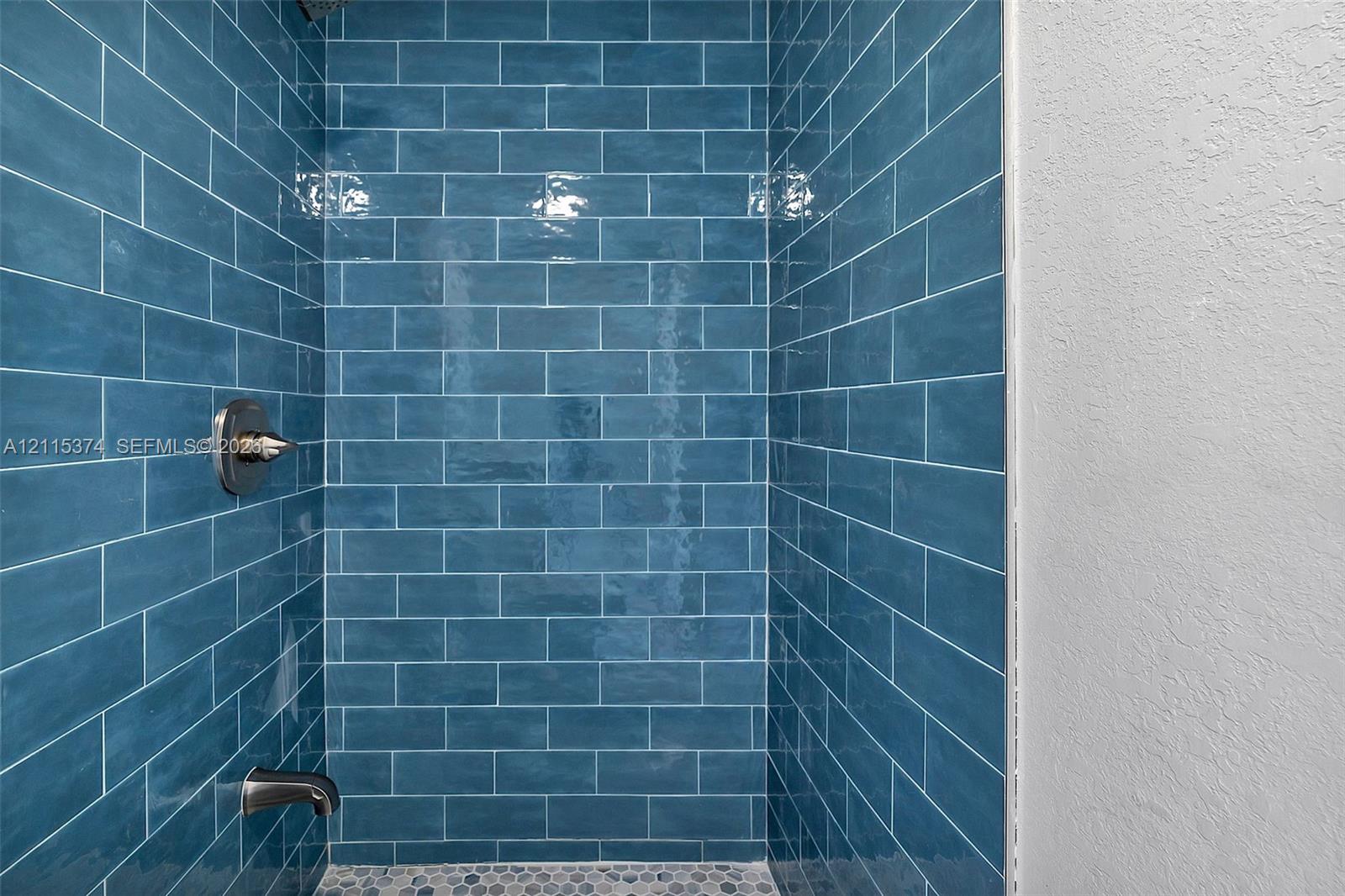 Shower stall featuring glossy blue subway tile wall surfacing, metallic faucet fixtures, and a natural stone pebble floor