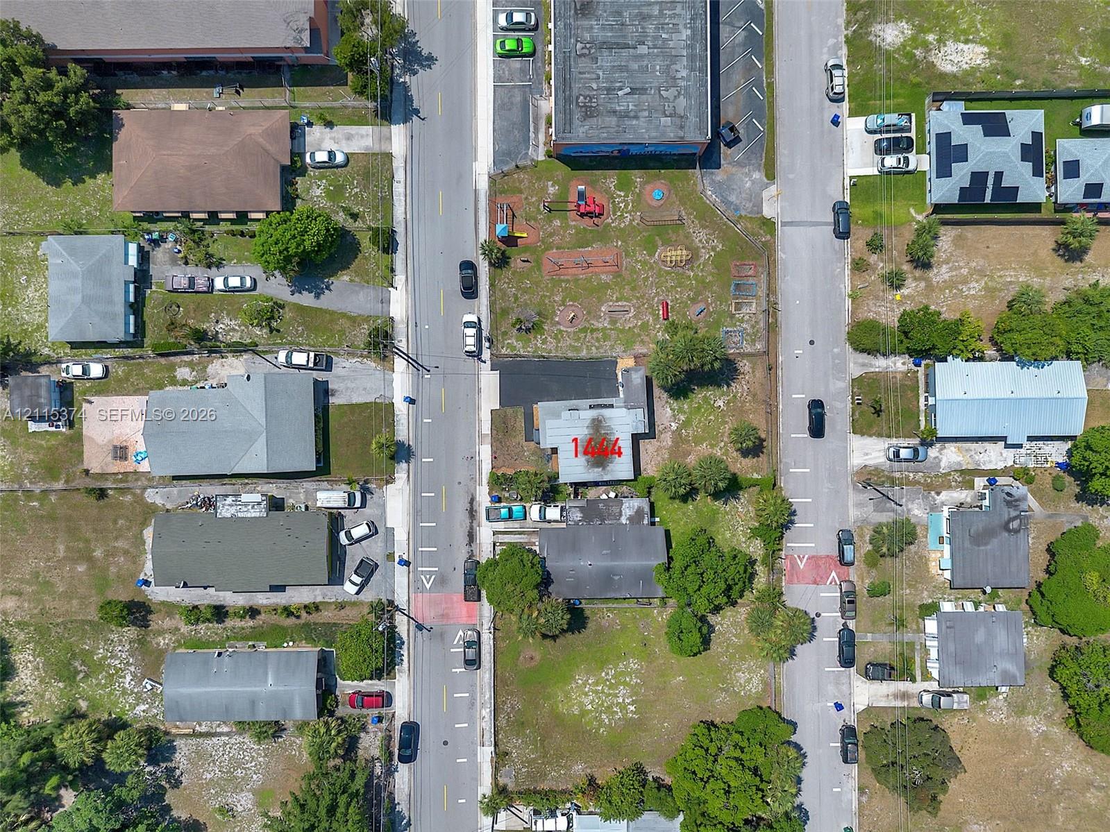 Aerial perspective of a property featuring a corner lot location, paved parking area, and established perimeter vegetation