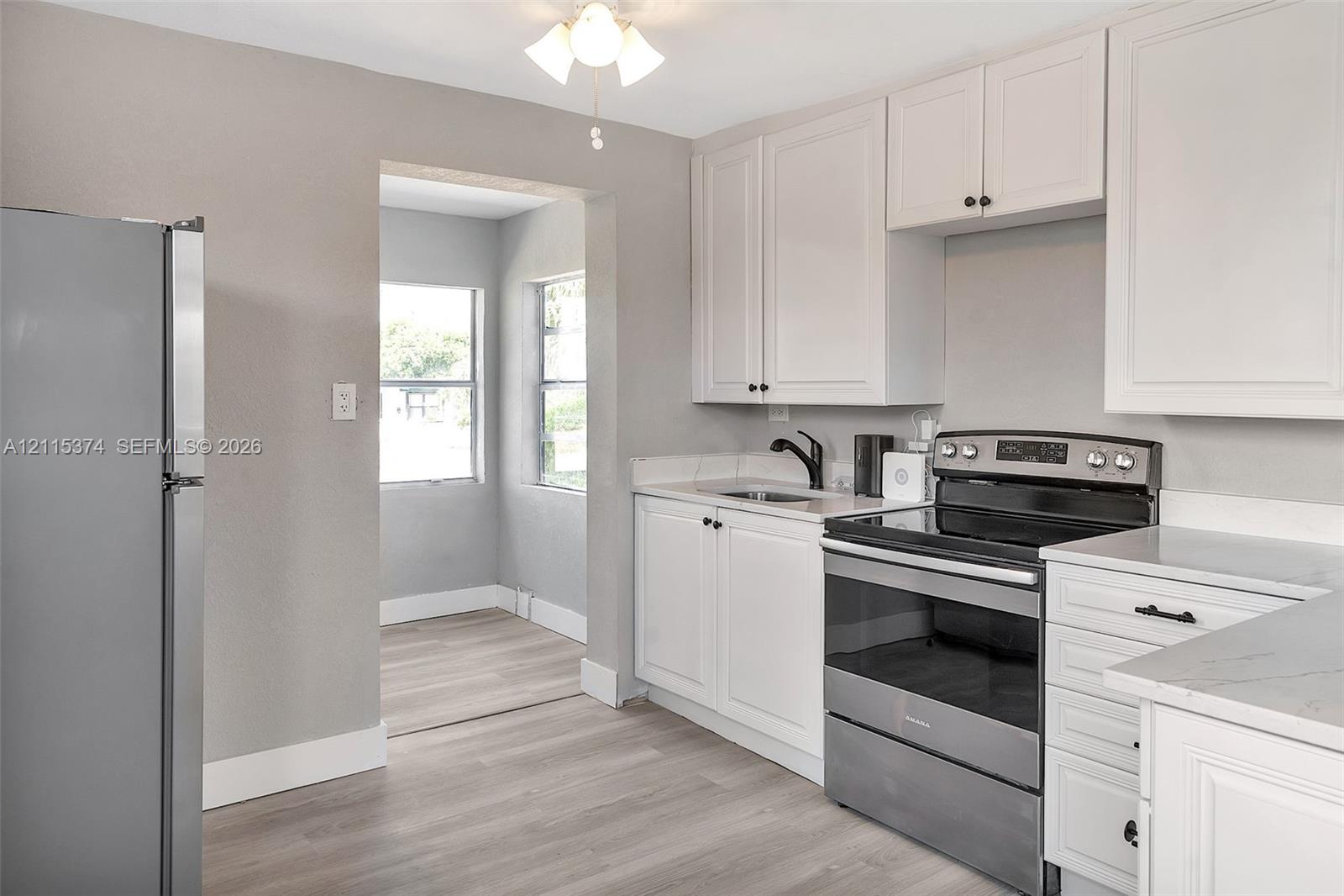 Kitchen featuring white shaker-style cabinetry, stainless steel appliances, light-toned stone-patterned countertops, a matte black faucet, and wood-finish flooring