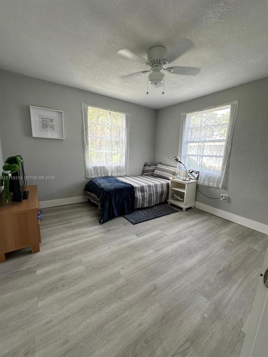 Room featuring wood-finish flooring, two windows with diamond-pattern muntins, and a ceiling-mounted light fixture with a fan