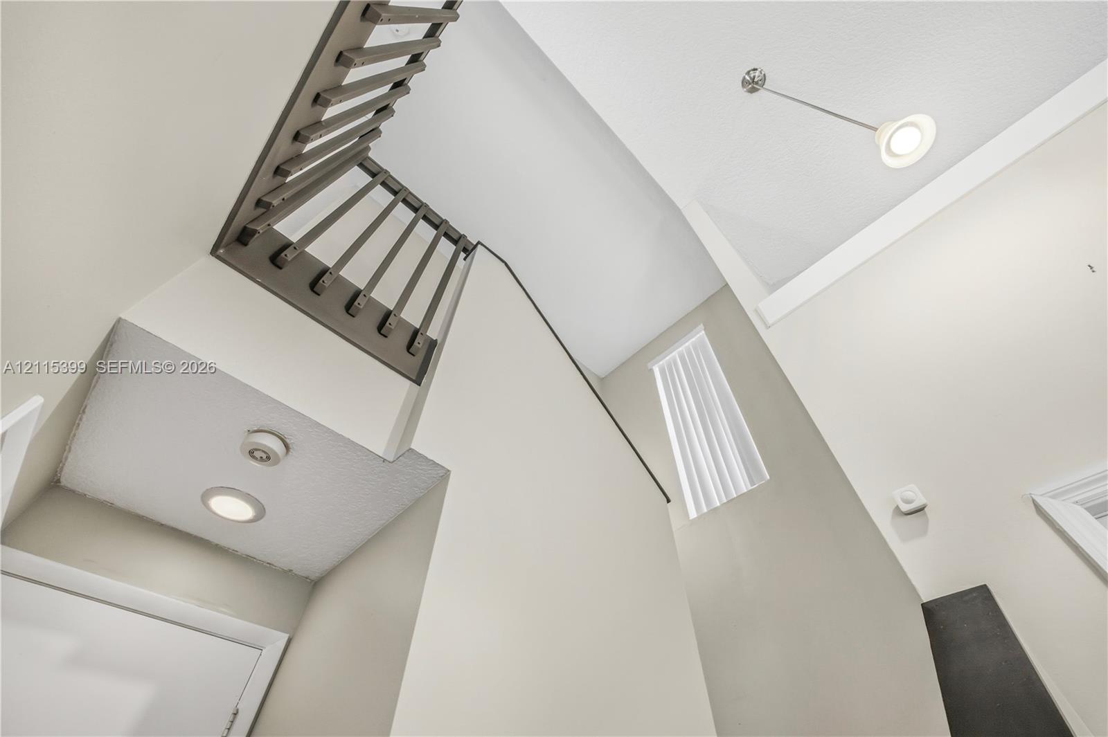 High-ceiling entryway featuring a staircase with dark-finished railings, vertical rectangular window, recessed lighting, and a pendant fixture
