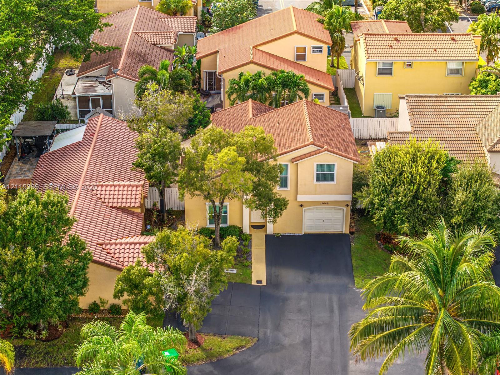 Two-story residence featuring a tile roof, paved driveway, single-car garage, and established landscaping