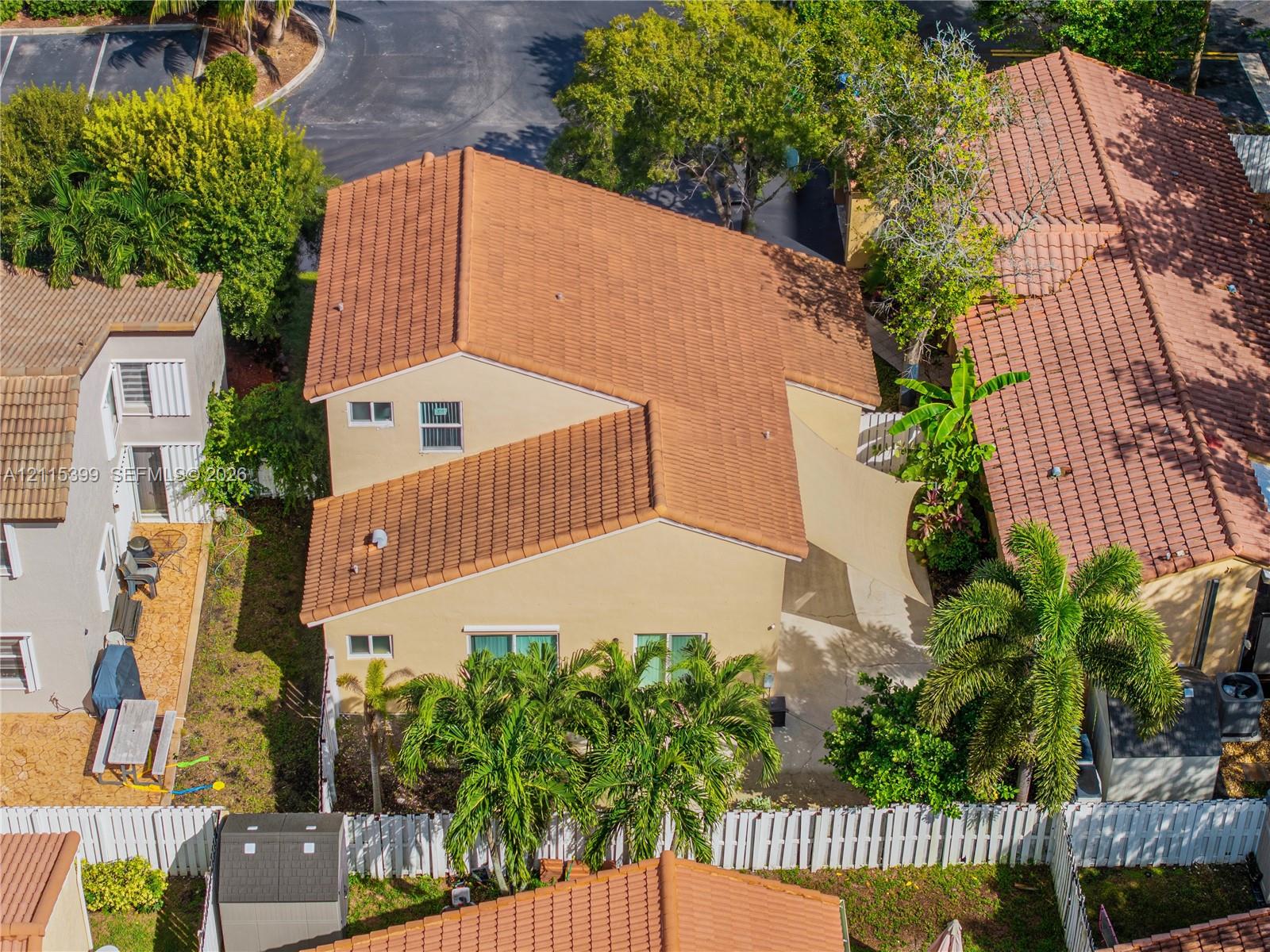 Stucco exterior featuring a terracotta tile roof, concrete patio, white vinyl fencing, and established palm landscaping