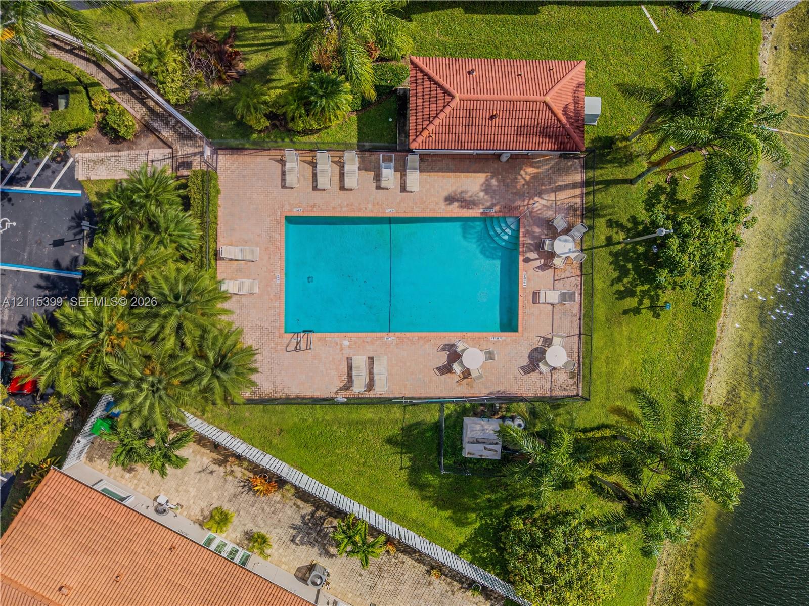 Rectangular swimming pool featuring a tile deck, attached covered structure with a terracotta-style roof, and perimeter fencing