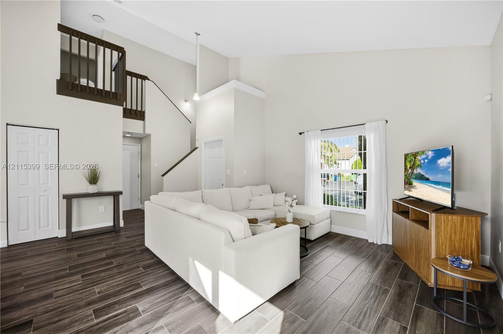 Living area featuring vaulted ceilings, wood-finish tile flooring, a mezzanine balcony with dark-finish railing, and a window with natural light