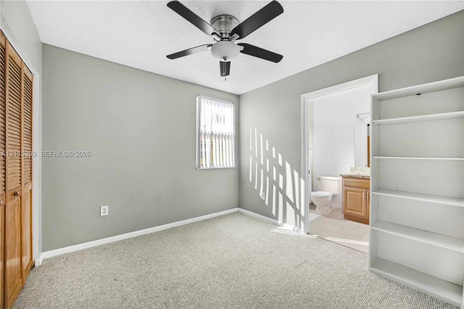 Neutral interior space featuring carpeted flooring, a ceiling fan, a window with vertical blinds, and a built-in wooden closet