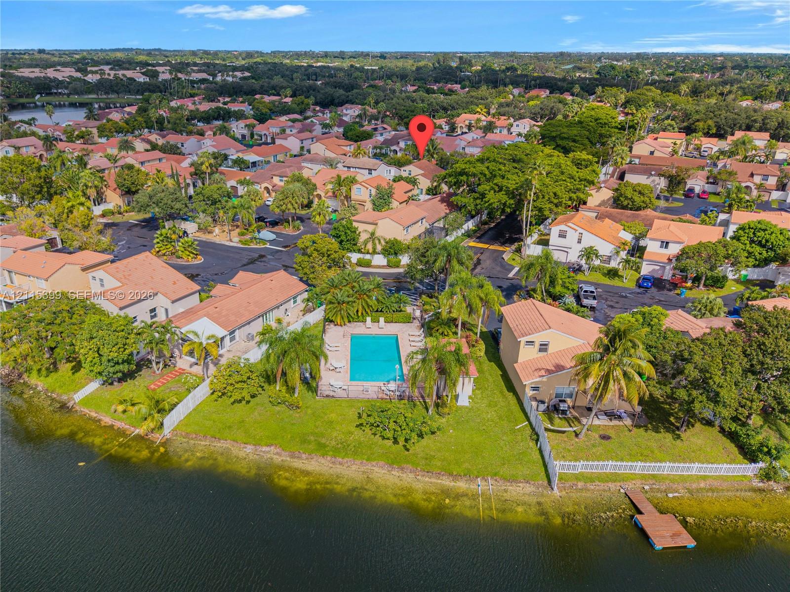 Aerial perspective of a waterfront property featuring a fenced swimming pool, private boat dock, green space, and mature landscaping