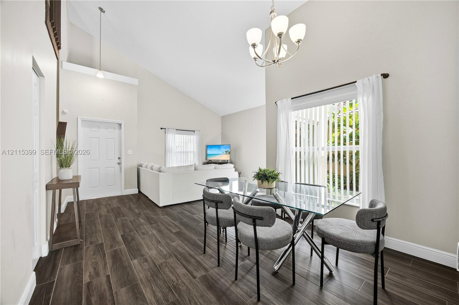 Vaulted ceilings, wood-finish flooring, multi-arm chandelier, and sliding glass door with vertical blinds