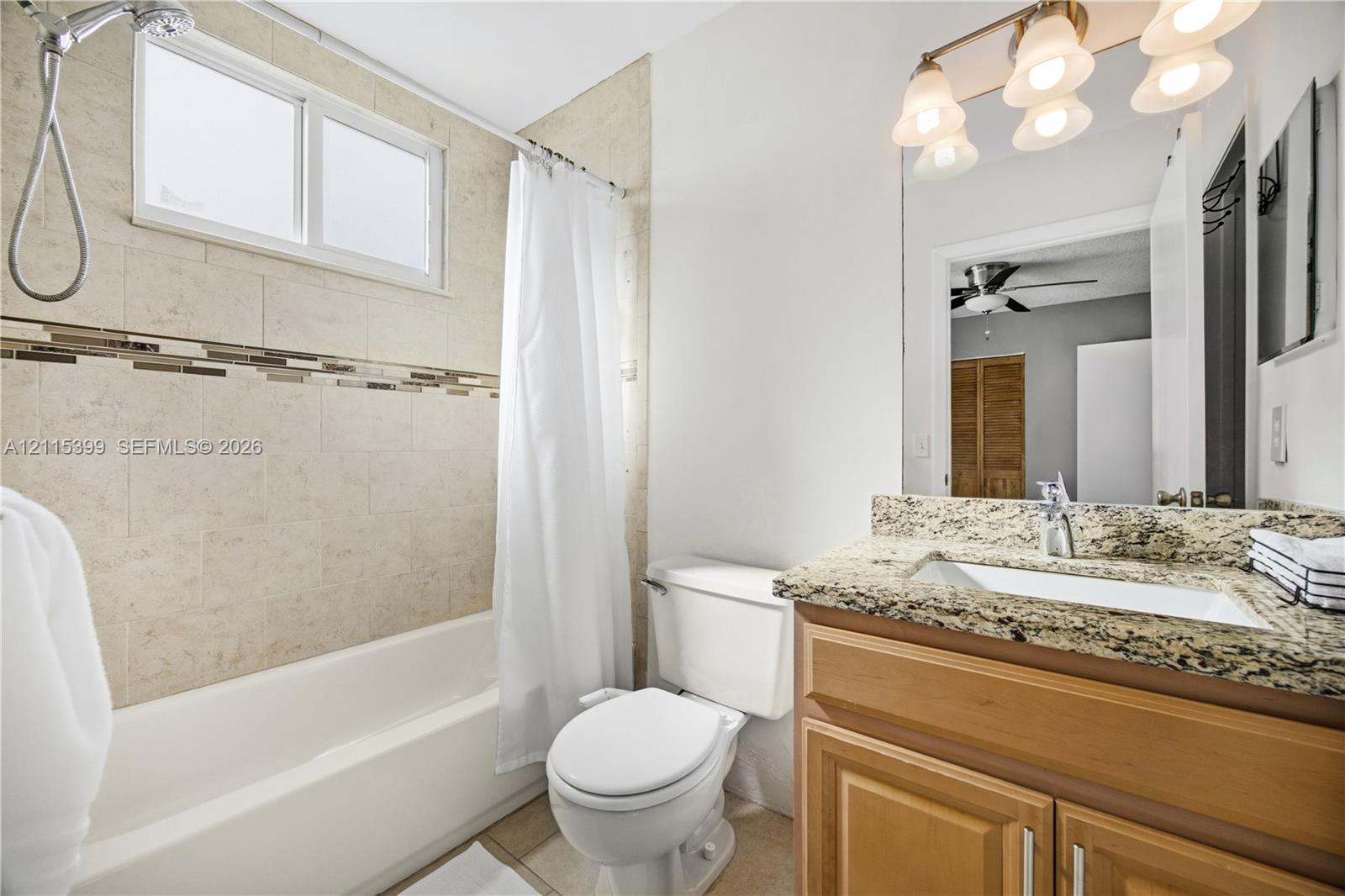 Bathroom featuring a vanity with a stone-finish countertop, undermount sink, multi-light fixture, tiled tub surround with decorative inlay, and a built-in shower faucet