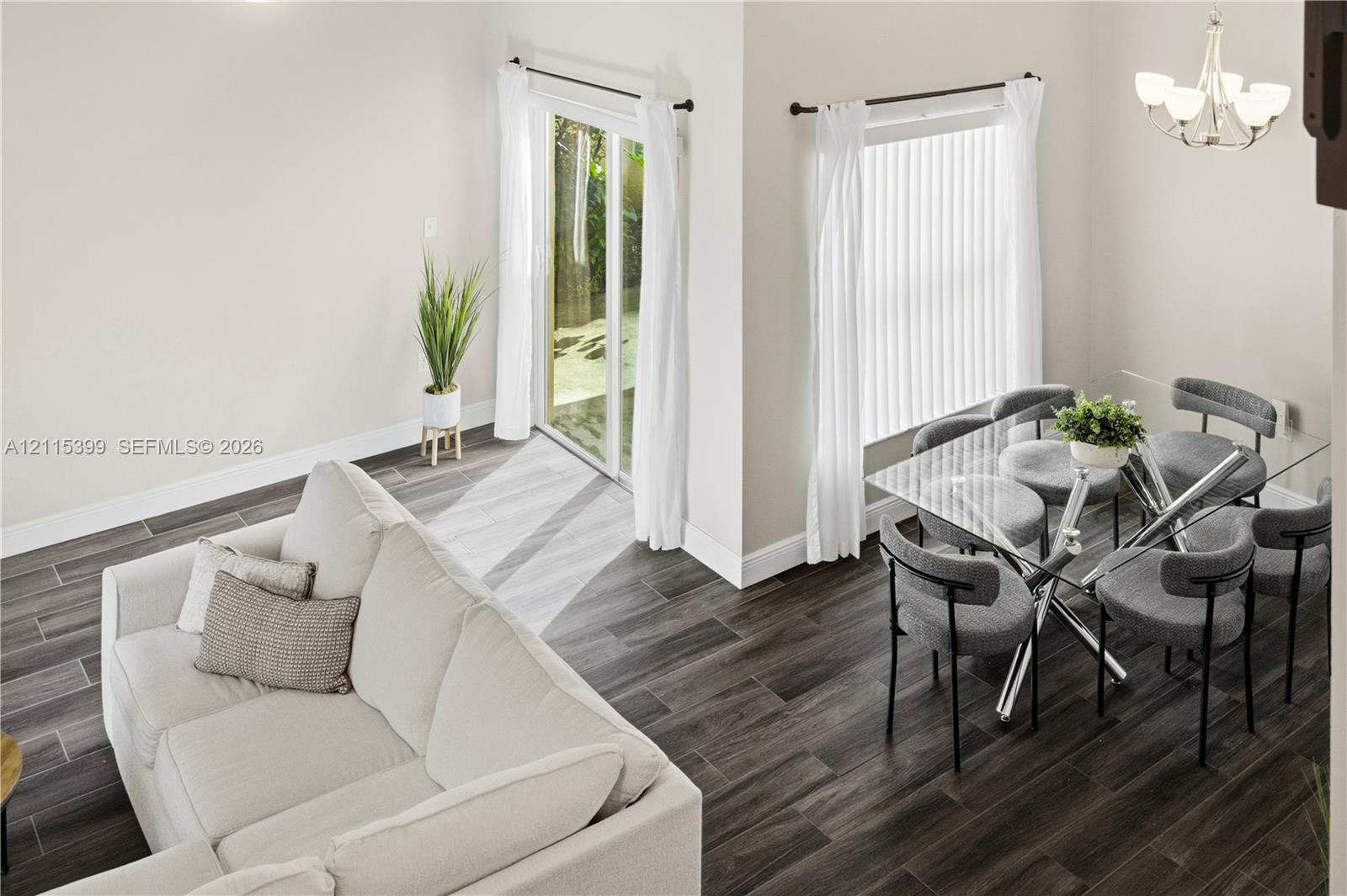 Open-concept interior featuring wood-finish tile flooring, vaulted ceilings, a sliding glass door, and a five-arm multi-light chandelier
